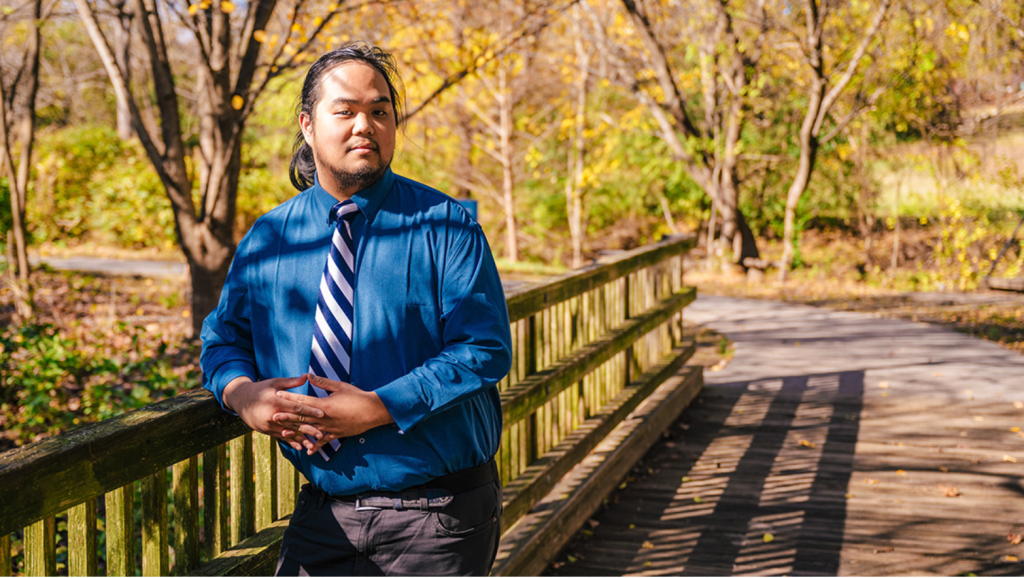 UNCG class of 2024 biology graduate Elijah Rusuello leans on a bridge